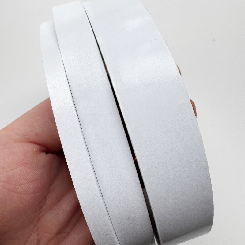A close-up of a hand holding a roll of white adhesive tape against a plain white background.