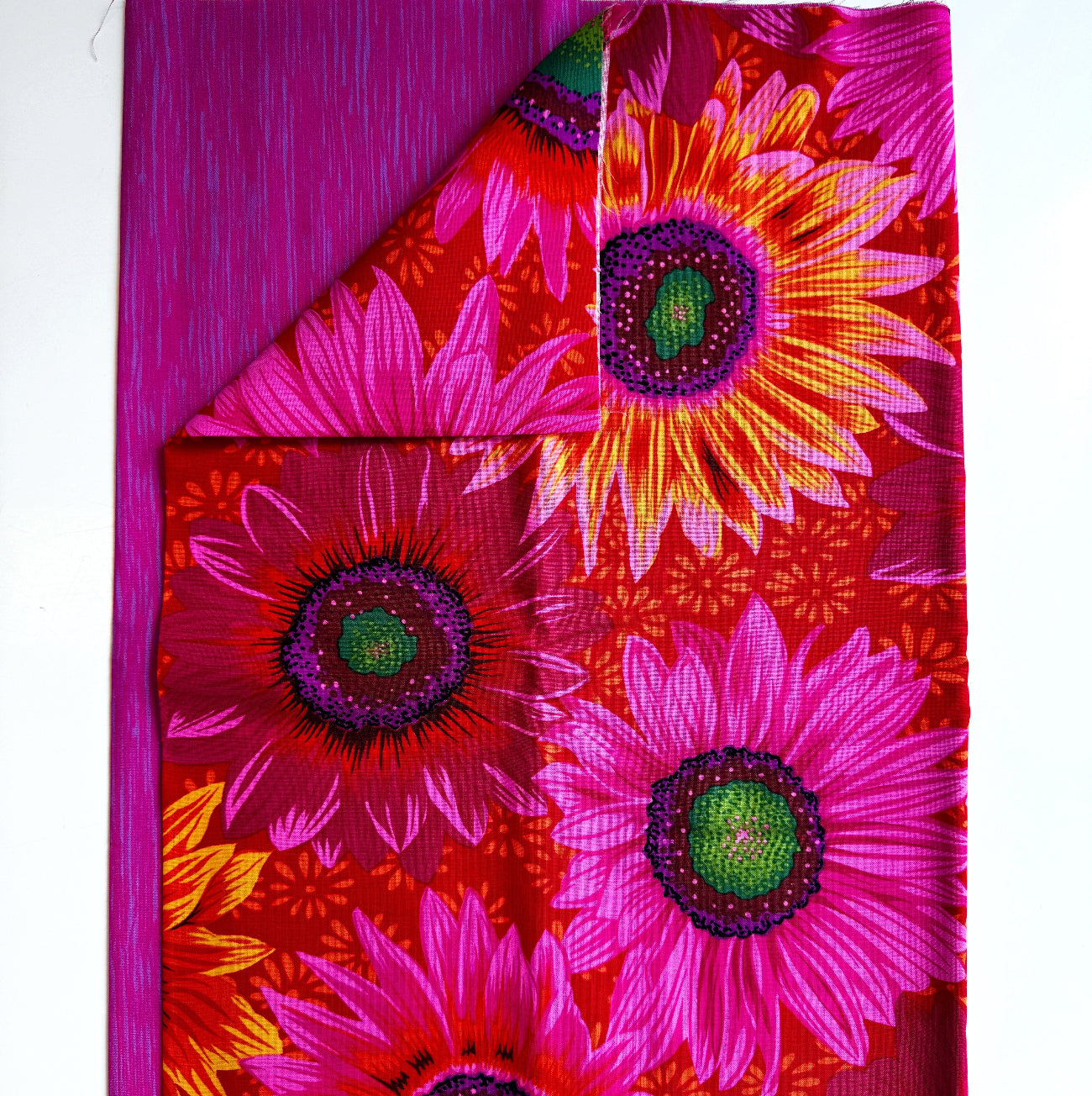 Large vibrant pink and orange sunflower print cotton fabric by Kaffe Fassett paired with a coordinating magenta pink textured tonal blender fabric for quilting and sewing.