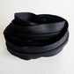 A coiled black zipper with a matching black pull tab, photographed on a plain light background.