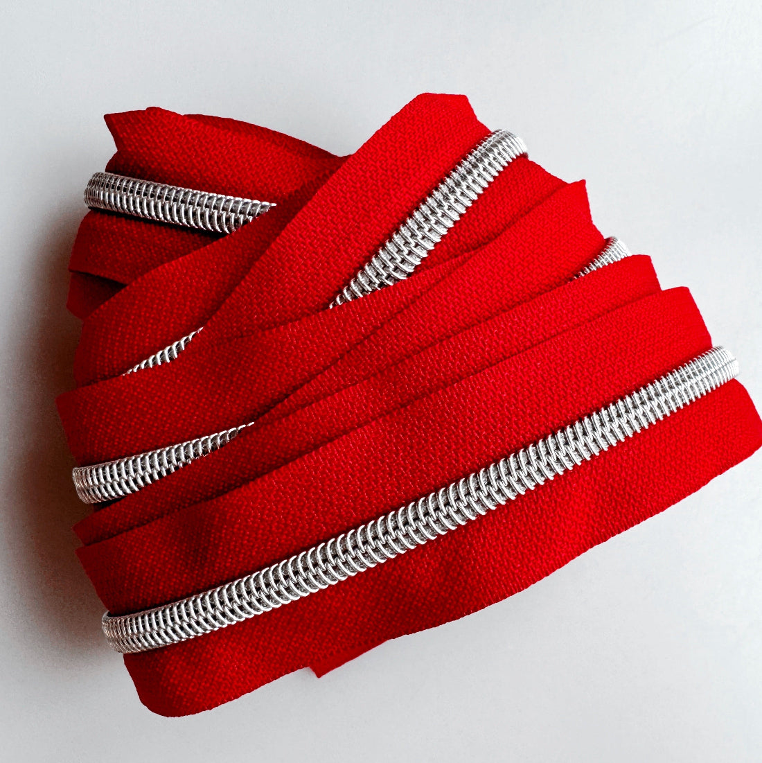A coiled bundle of bright red zipper tape with silver metal teeth, photographed on a plain light background.