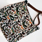 A fabric shoulder bag with an all-over vintage-style butterfly print on a white background, featuring a brown leather strap and a small front pocket.