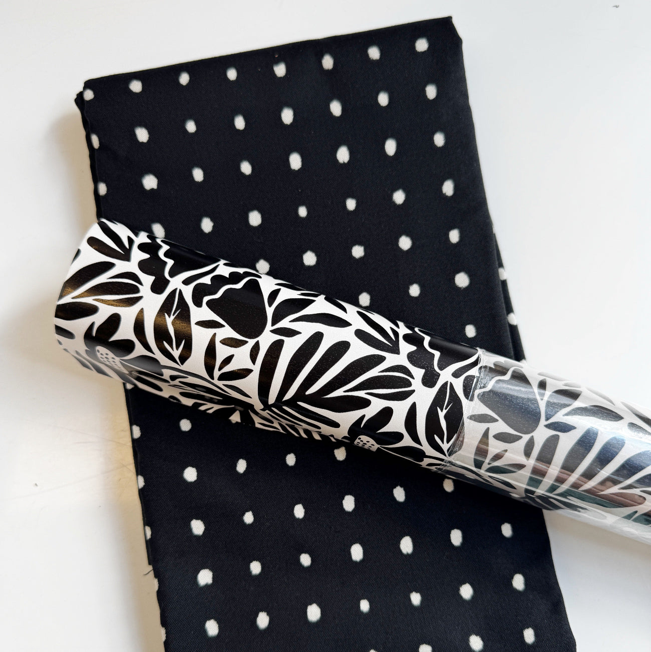 Black and white polka dot cotton fabric paired with a matching bold black and white floral botanical patterned vinyl roll for handmade bag making and sewing projects.