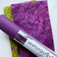 A flat-lay view of the craft materials for the Match Up #2 package, showing a piece of yellow floral fabric, a piece of purple dot-patterned fabric, and a roll of purple textured vinyl labeled "sewhungryhippie".
