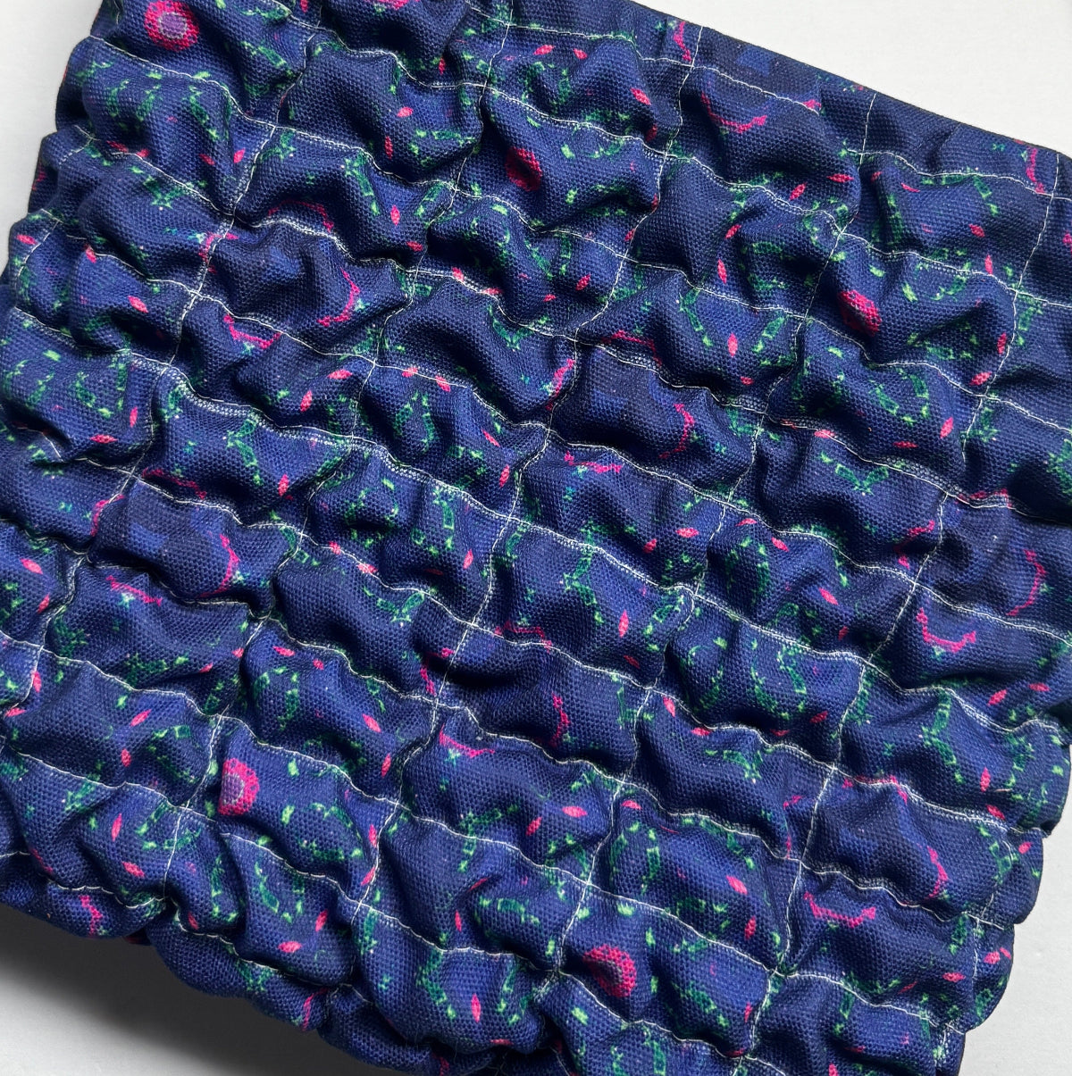 Stack of blue fabric with pink and green patterns on a white background