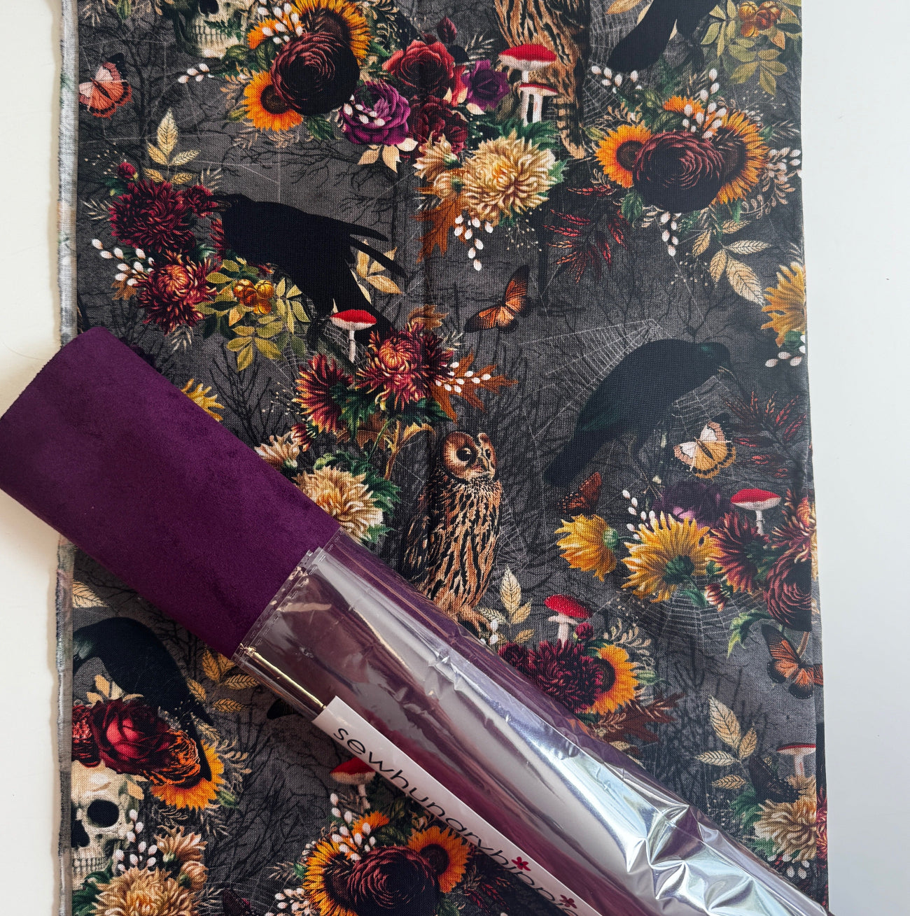 A spooky autumn-themed craft bundle with skull, mushroom, and crow print fabric alongside a roll of rich violet faux leather vinyl