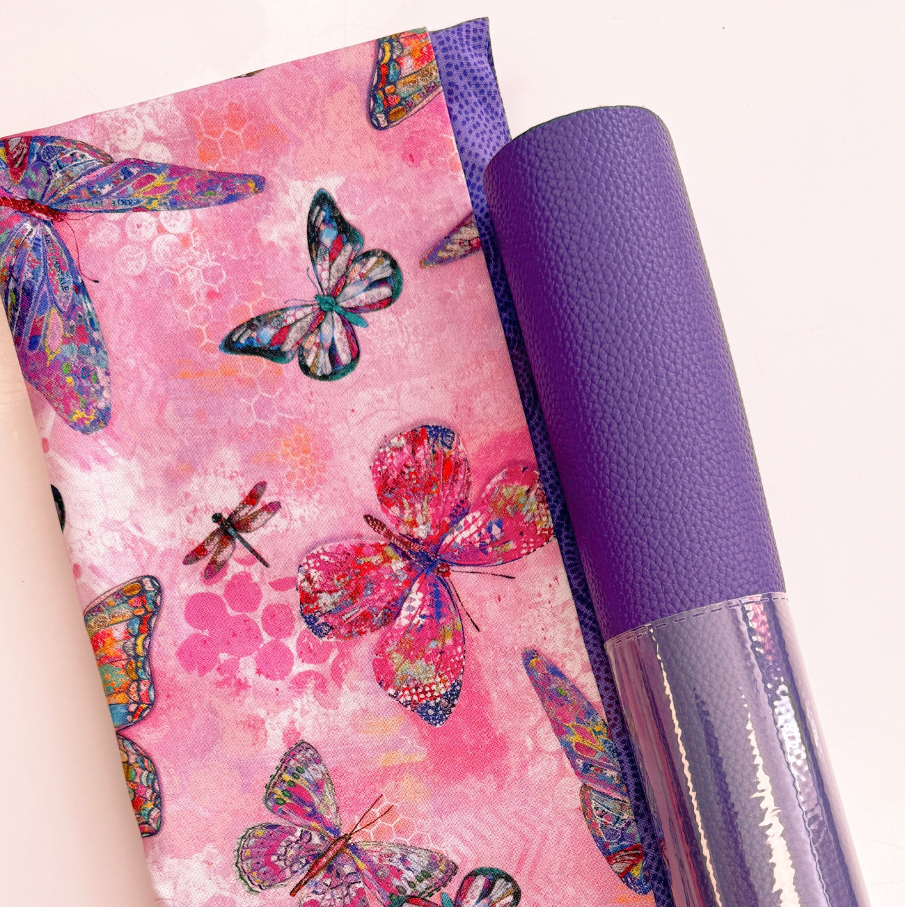 A flat-lay view of the craft materials for the Match Up #7 package, showing a folded piece of pink fabric with a butterfly and dragonfly print next to a roll of purple textured "Moonglow" vinyl.