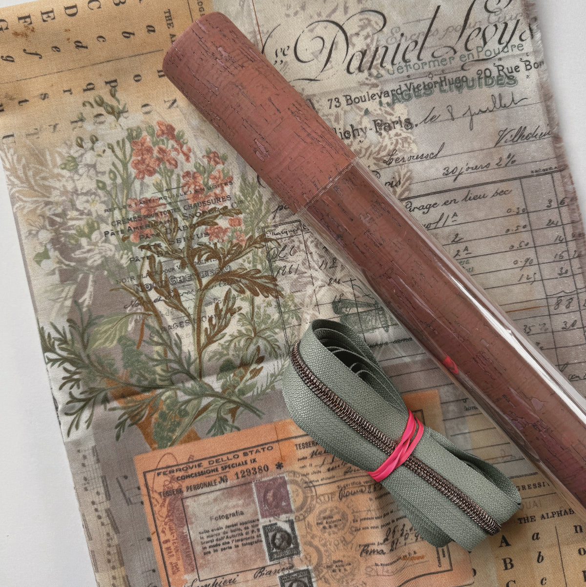 Roll of brown paper and green fabric with a zipper on top of vintage documents.