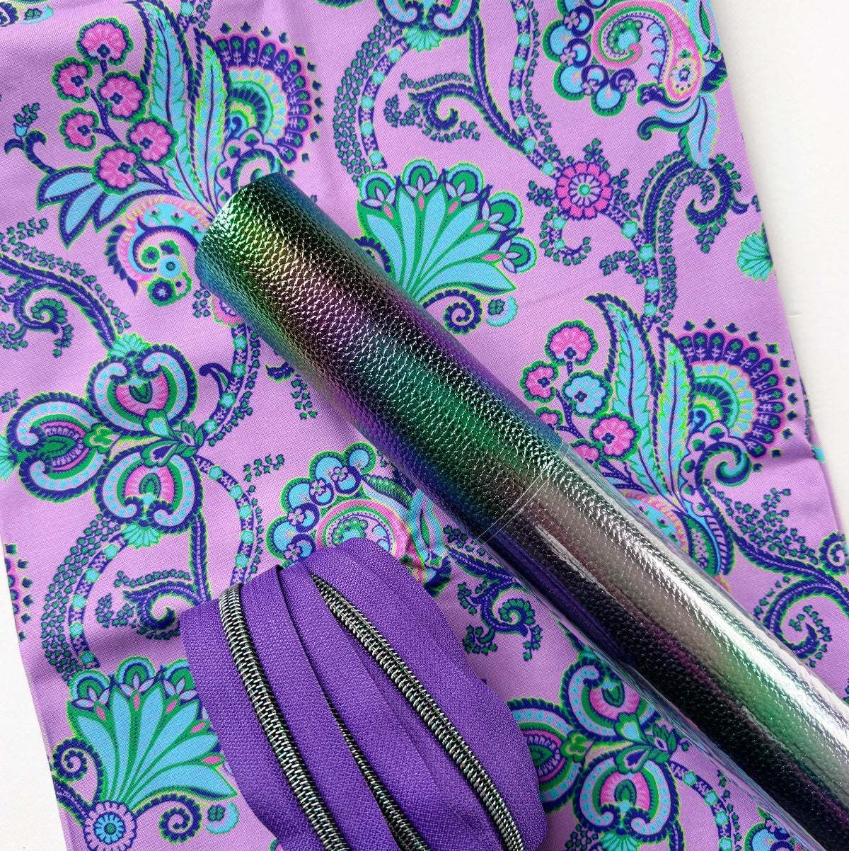 Purple paisley-patterned fabric with a metallic pen and purple pouch on top