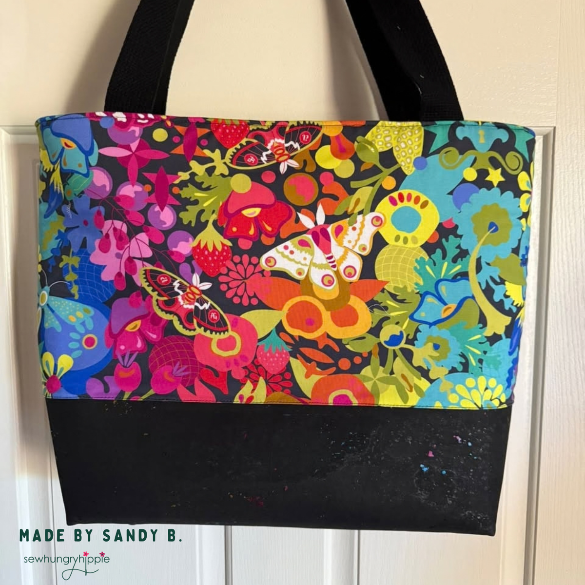 Tote bag in Alison Glass Art Theory Night wideback with colorful moths and flowers on black, with a black cork base