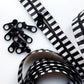 Black and white striped zipper ribbon with black metal zipper teeth, shown coiled on a white background with several loose zipper teeth pieces.