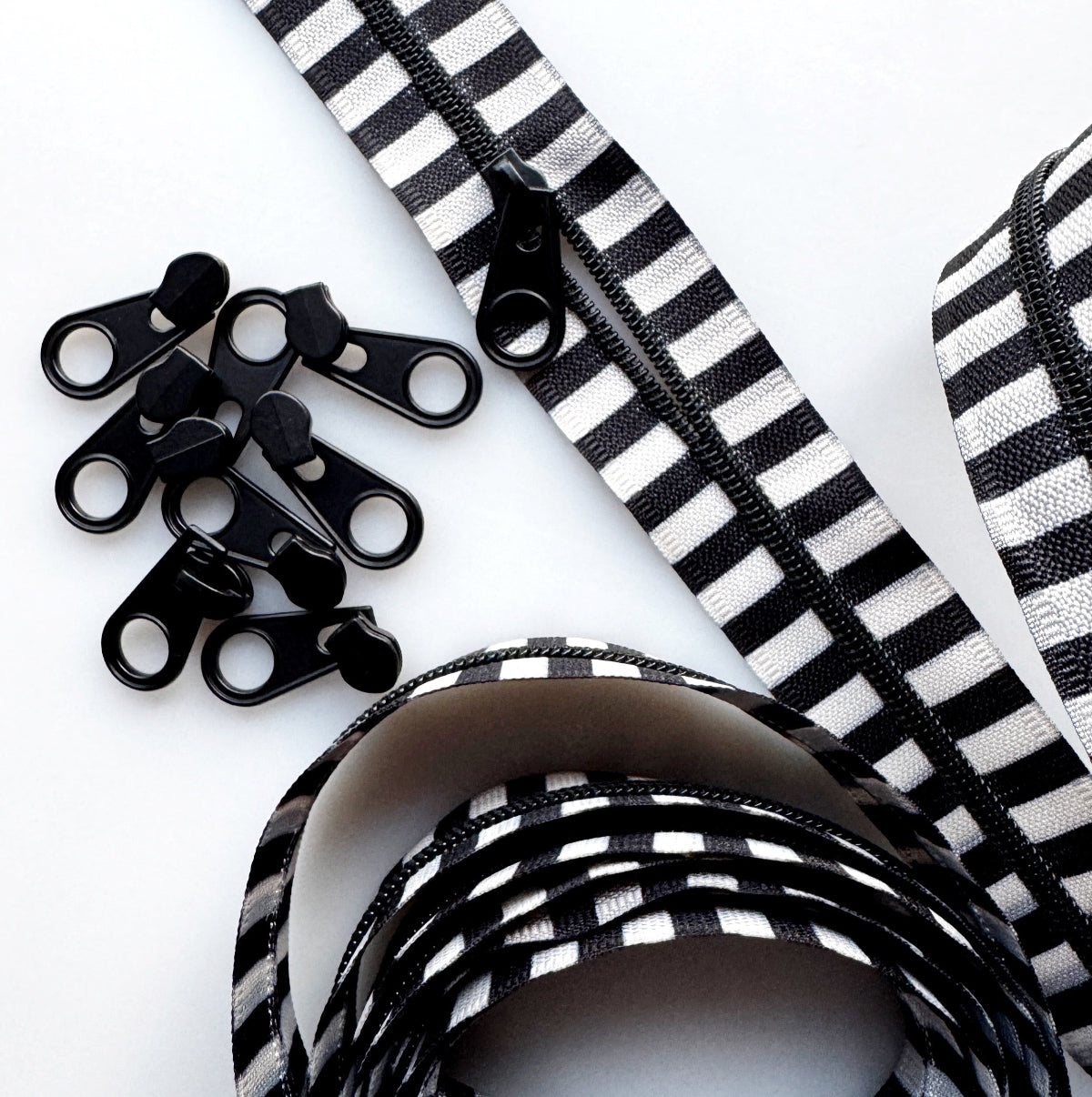 Black and white striped zipper ribbon with black metal zipper teeth, shown coiled on a white background with several loose zipper teeth pieces.