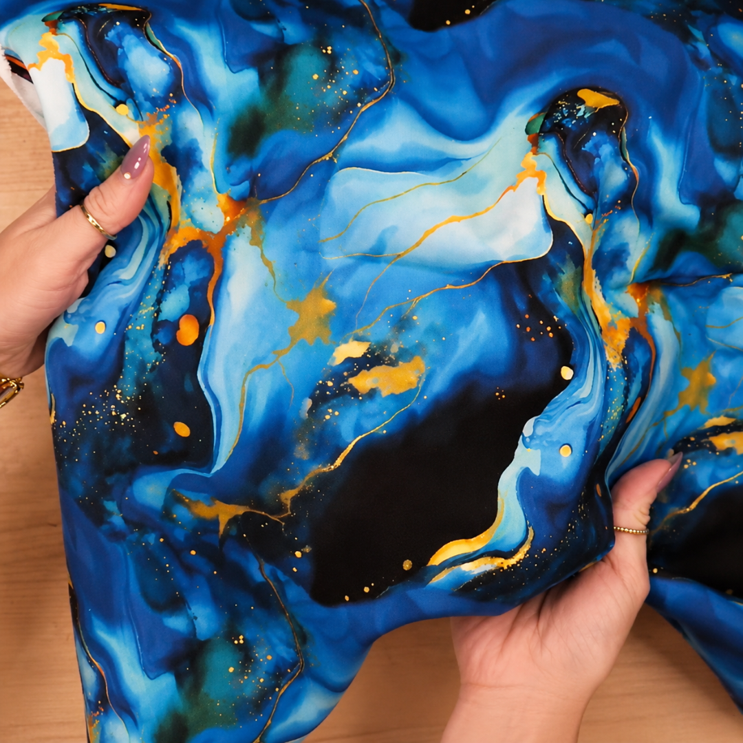 Blue and gold marbled fabric held by hands on a wooden surface