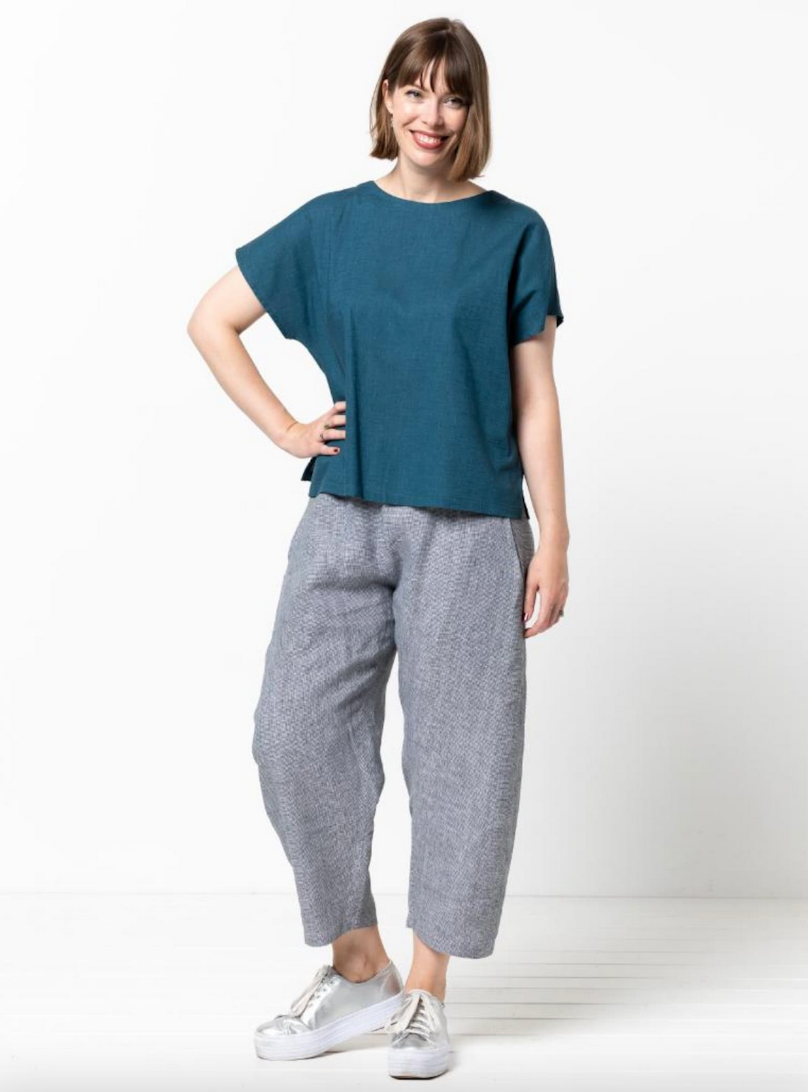 Woman wearing a teal top and gray pants on a white background