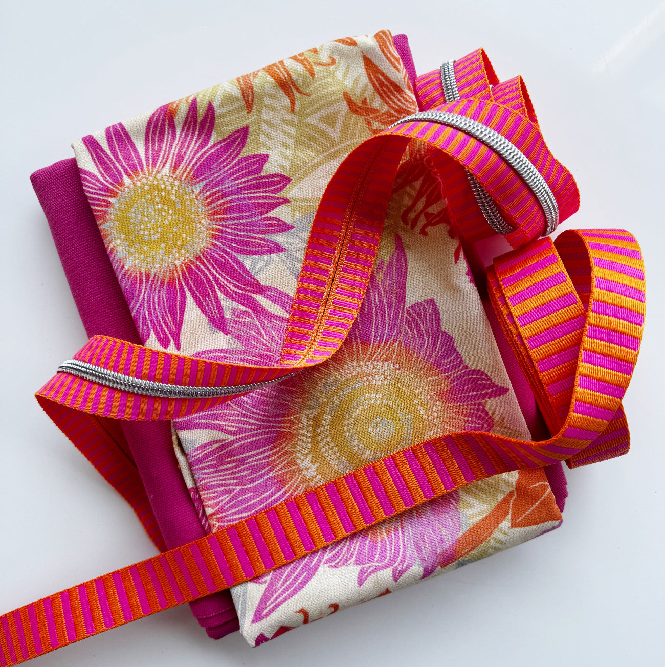 A flat-lay view of the craft materials for the Match Up #5 package, consisting of folded magenta and floral-print canvas fabric, a coil of orange and pink striped webbing, and a length of silver zipper.