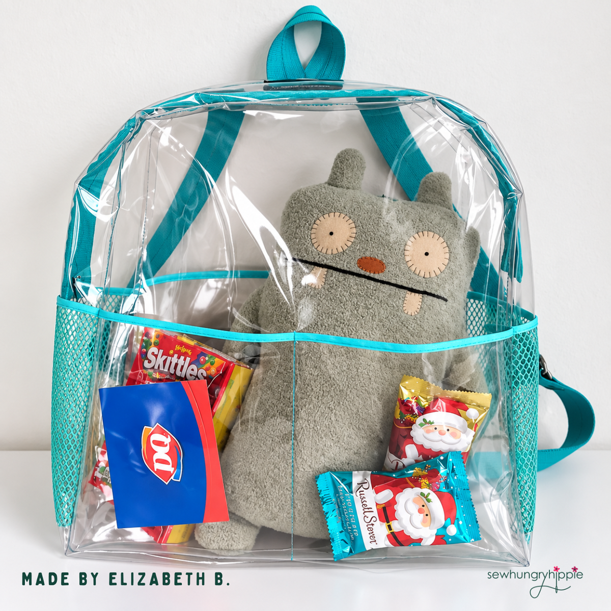Clear vinyl backpack with teal binding and mesh side pockets holding a plush toy and snacks, made by Elizabeth B.