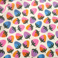 A close-up of a fabric or paper material featuring a colorful repeating strawberry pattern on a cream background.