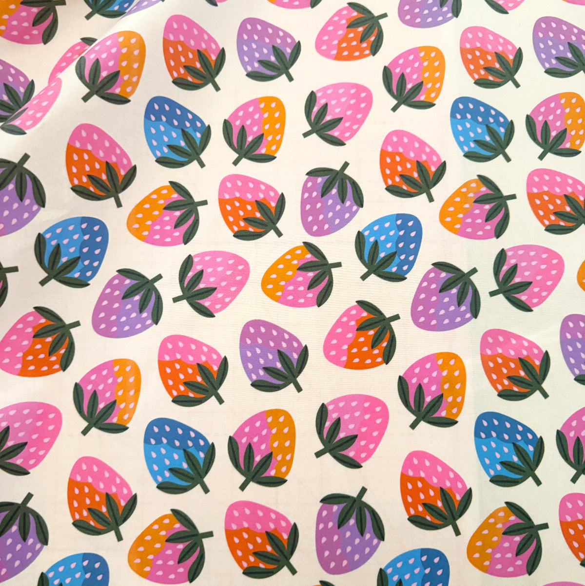 A close-up of a fabric or paper material featuring a colorful repeating strawberry pattern on a cream background.