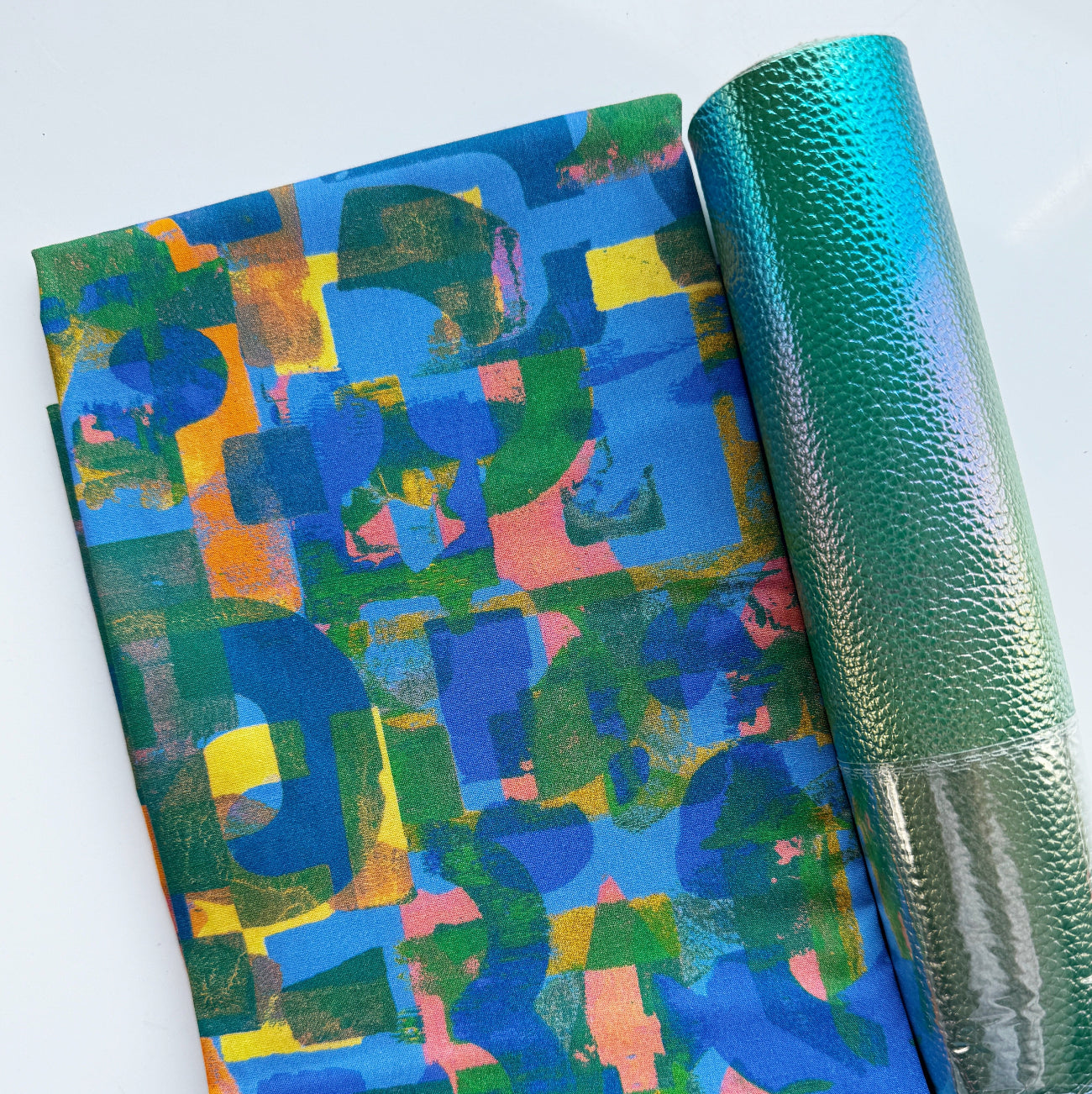 A flat-lay view of the craft materials for the Match Up #1 package, featuring a folded piece of blue fabric with an abstract geometric pattern next to a rolled sheet of textured teal "Moonglow" vinyl.