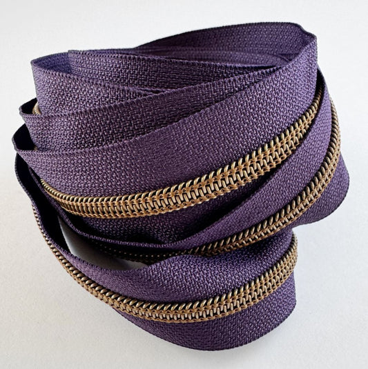 A textured roll of dark purple fabric zipper tape featuring a metallic gold-tone nylon coil.