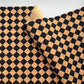 A close-up of a black and tan checkered pattern, likely cork or cork-like material, folded over to show the reverse side on a light gray background.