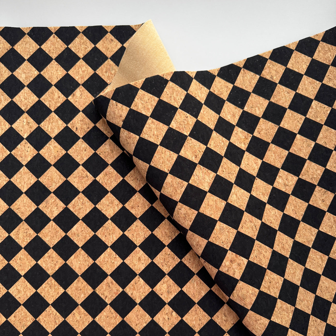 A close-up of a black and tan checkered pattern, likely cork or cork-like material, folded over to show the reverse side on a light gray background.