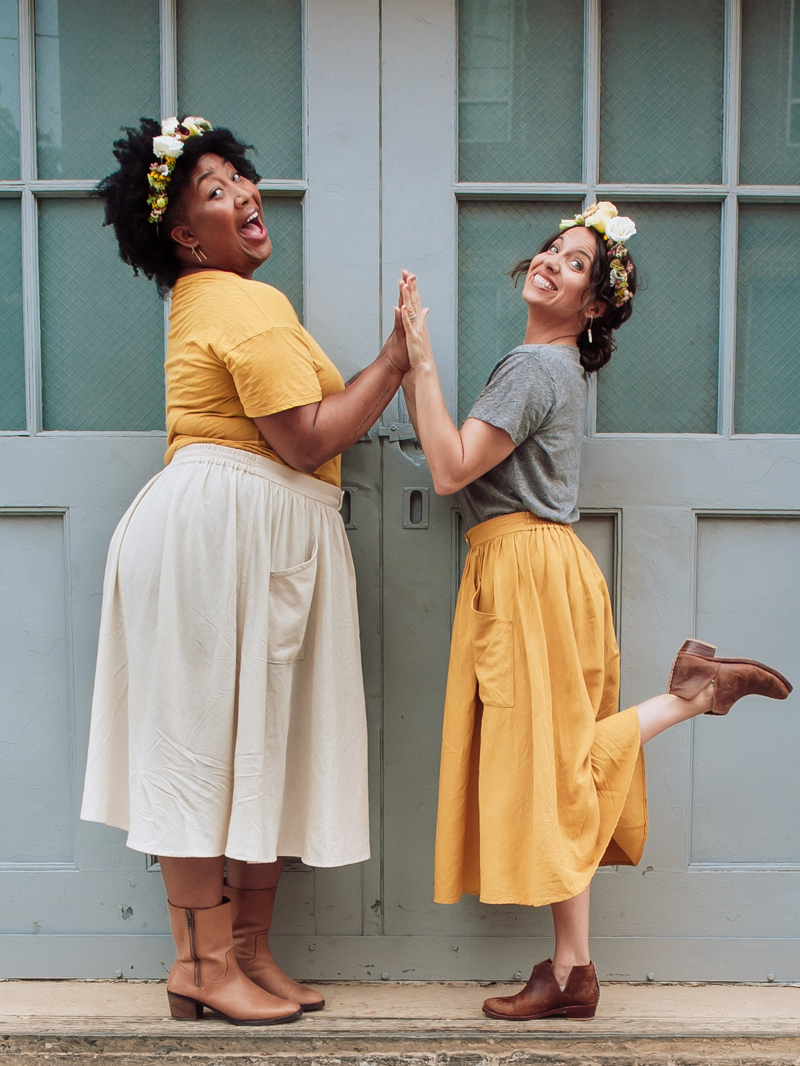 Two women standing on a step, wearing matching outfits with yellow and gray shirts and beige skirts.
