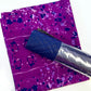 A flat-lay view of the craft materials for the Match Up #6 package, showing a piece of purple fabric with a splatter paint design next to a roll of blue pre-quilted, pebbled vinyl.