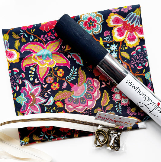 Sewing kit or bag-making supply bundle from Sew Hungryhippie, featuring a dark floral print fabric, a roll of navy blue cork  a white zipper tape in bronze teeth, and  bronze hardware d-rings and shivels.