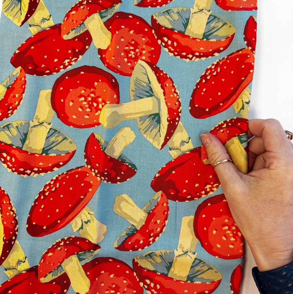 Hand holding fabric mushroom print in blue background by FreeSpirit Forage Toadstool Fabric