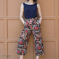 Person wearing a navy top and patterned pants against a brown paneled wall.