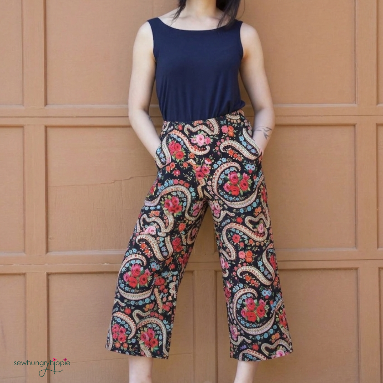 Person wearing a navy top and patterned pants against a brown paneled wall.