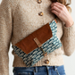 Person wearing a beige sweater with a brown and patterned waist bag.