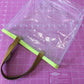 Clear tote bag with brown handle.