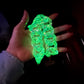 Hand holding a glowing green, UV-reactive clear acrylic chunky chain link accessory under a blacklight.