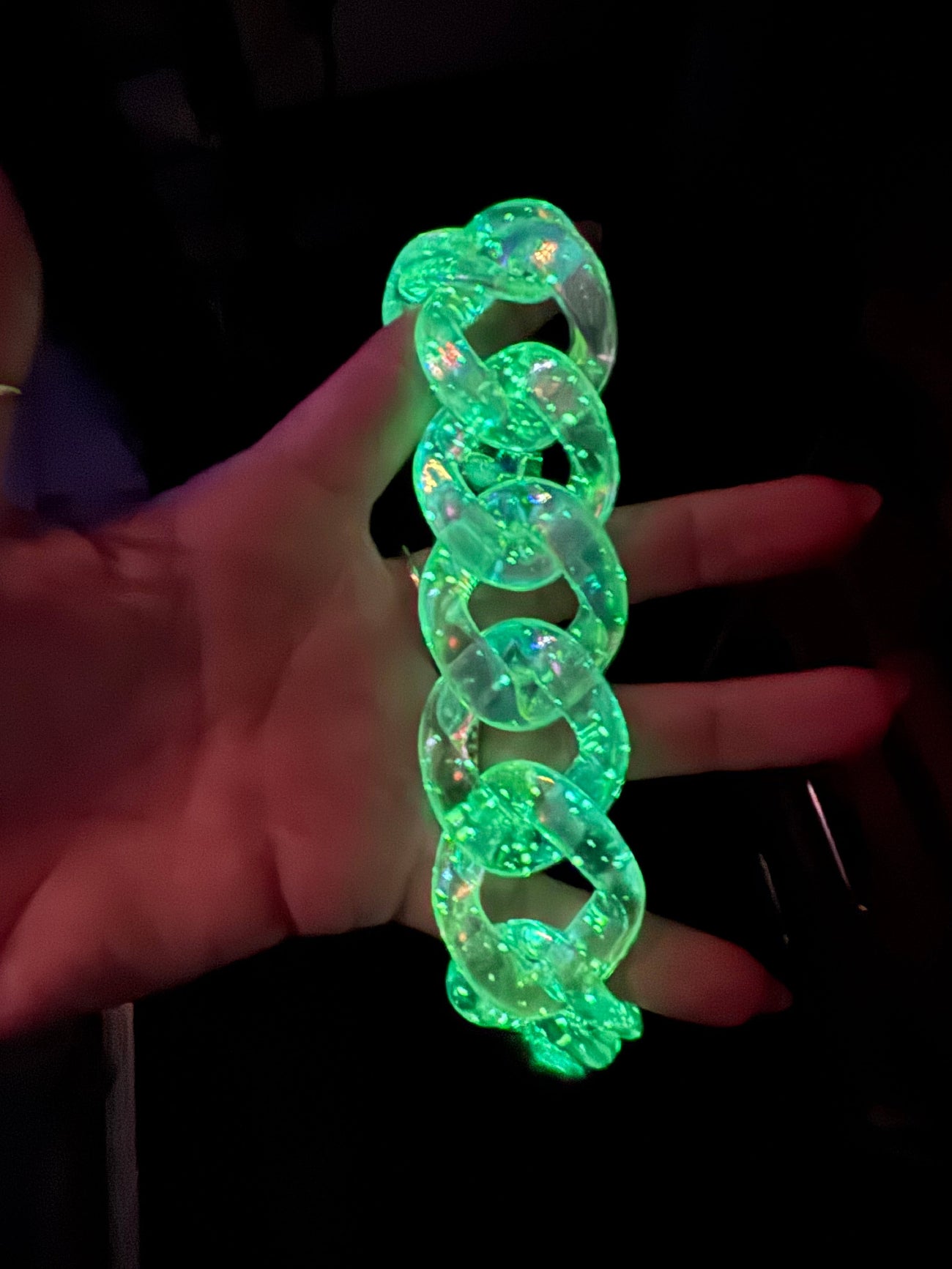 Person holding a folded neon green glow-in-the-dark chunky plastic chain bag strap or necklace under UV light.