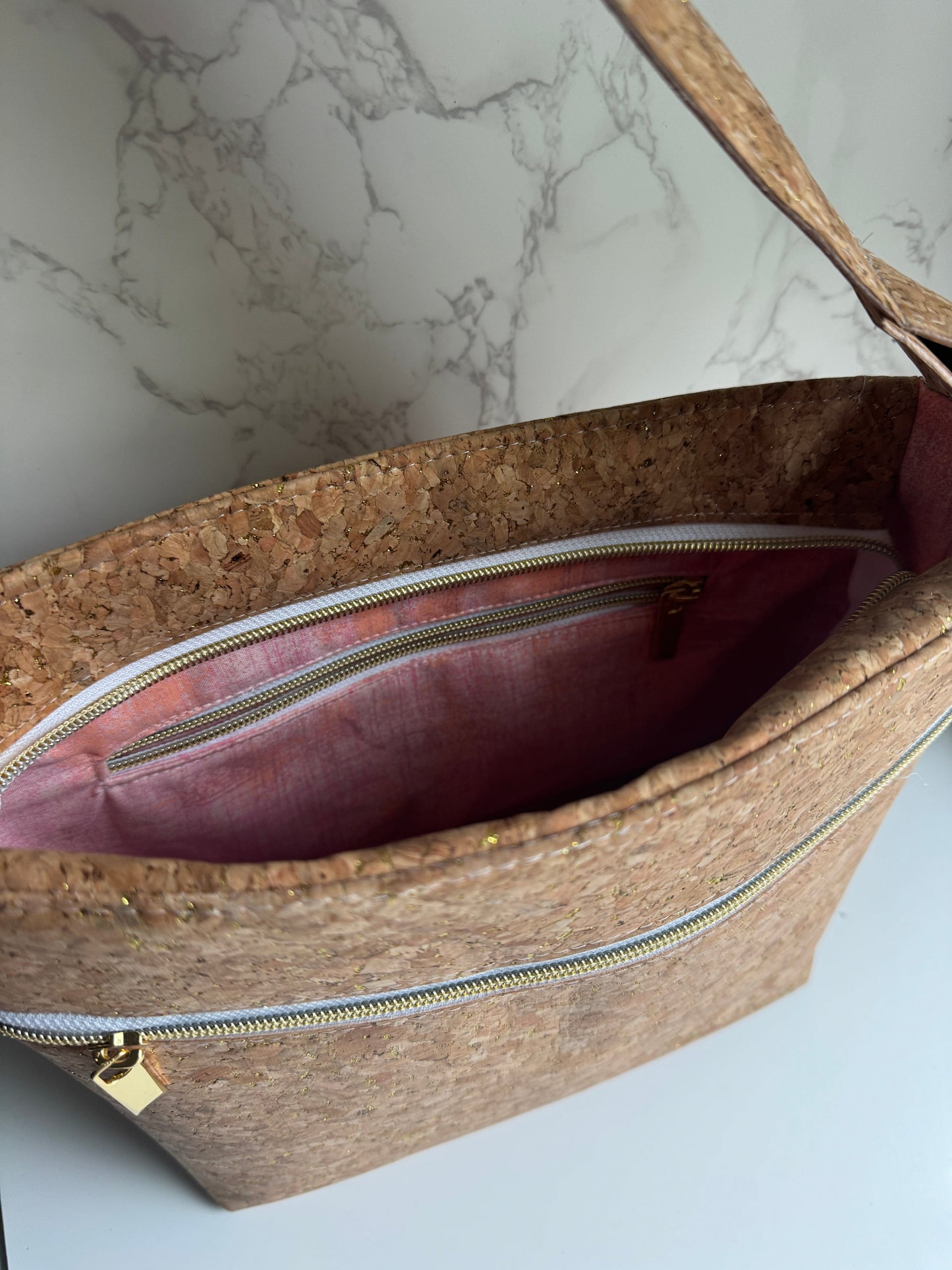 Cork handbag with zipper and pink interior against marble background.