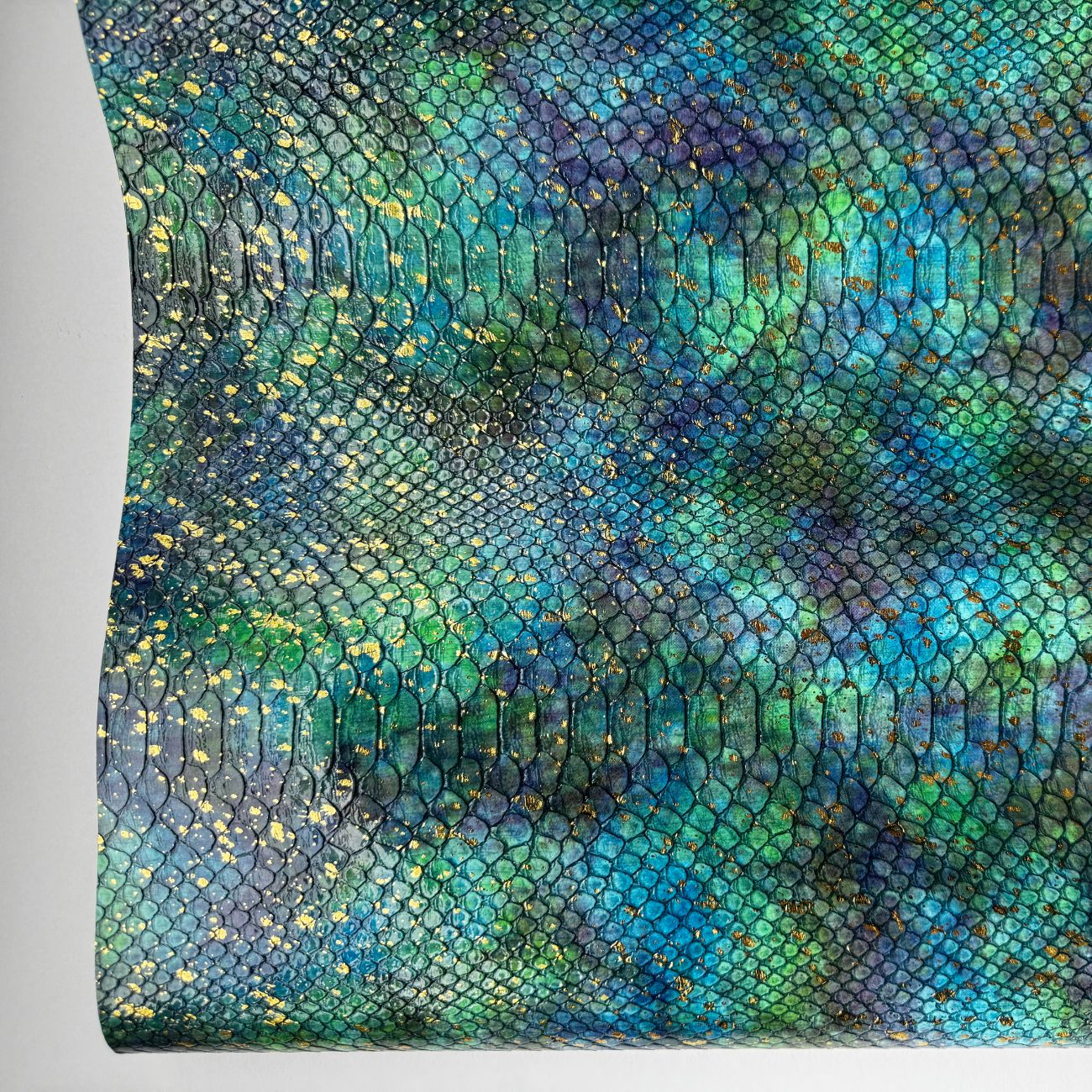 Teal and blue embossed serpent vinyl with a scale texture and gold foil accents. This shimmering faux leather is perfect for high-end bag making.