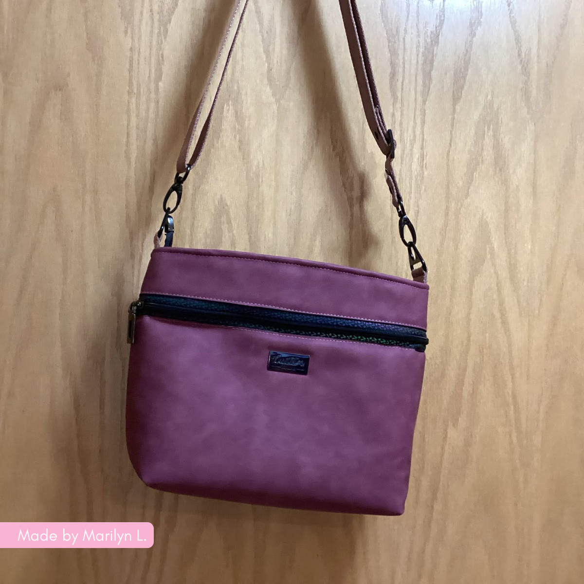 A small magenta crossbody bag with a shoulder strap hanging against a wooden door.