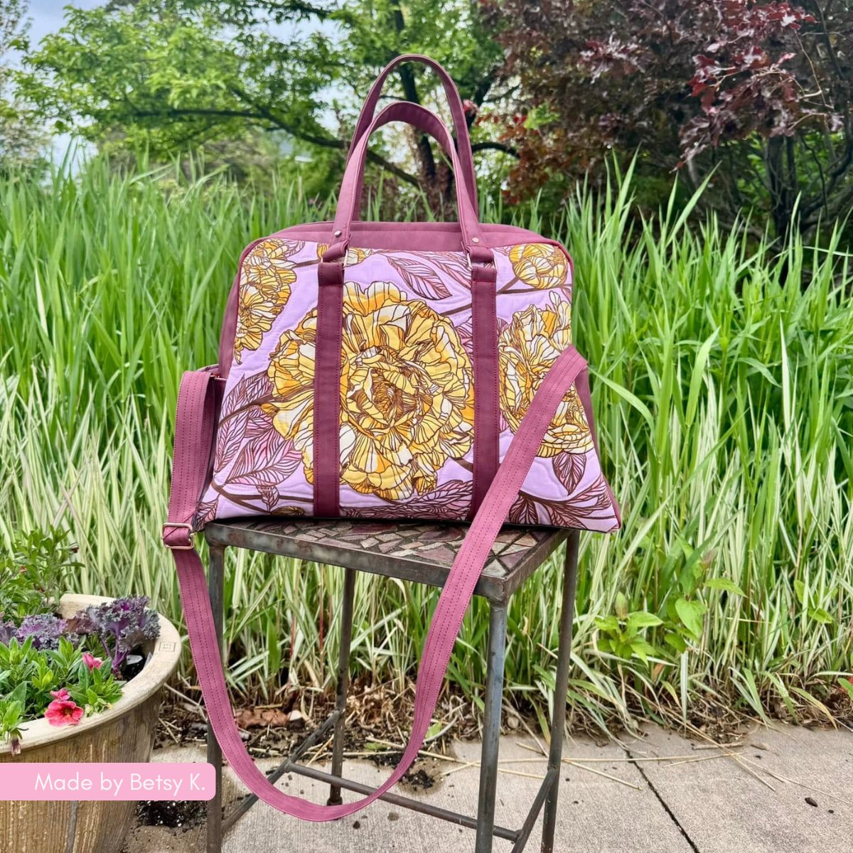 A larger magenta handbag with decorative floral pattern panels, resting on a stand outdoors with greenery in the background.