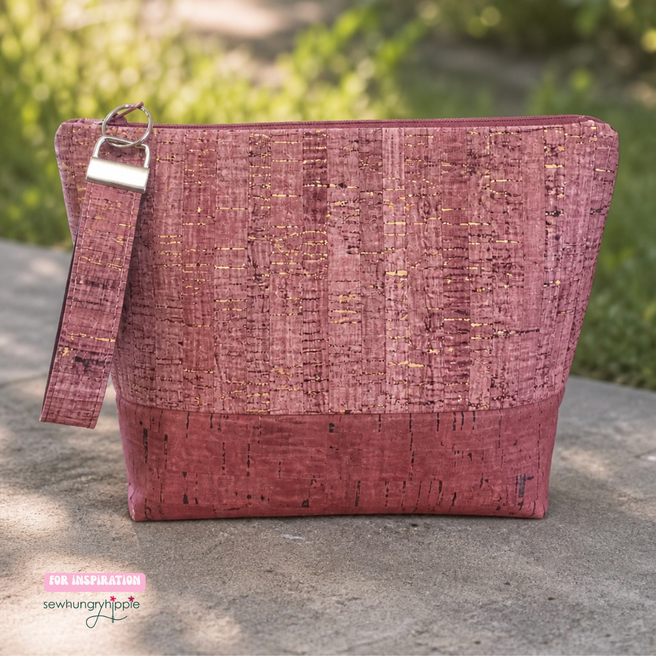 Handmade mauve cork fabric zipper pouch with a matching wristlet strap and gold metallic flecks, displayed outdoors on a concrete surface.