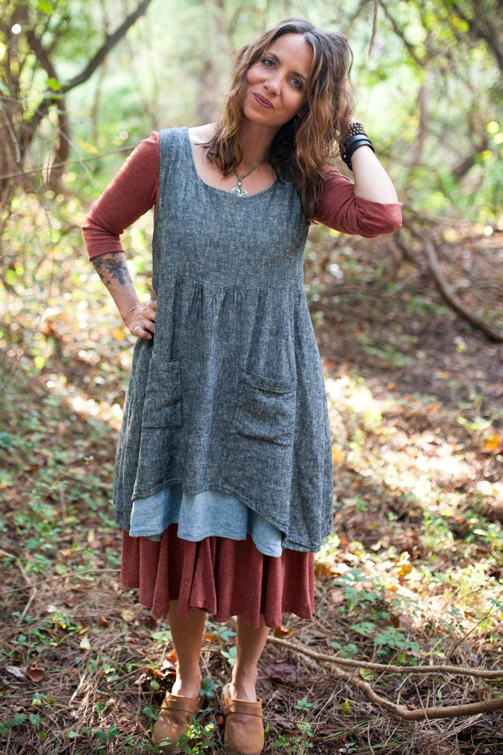 Woman wearing a gray dress over a red dress in a forest setting