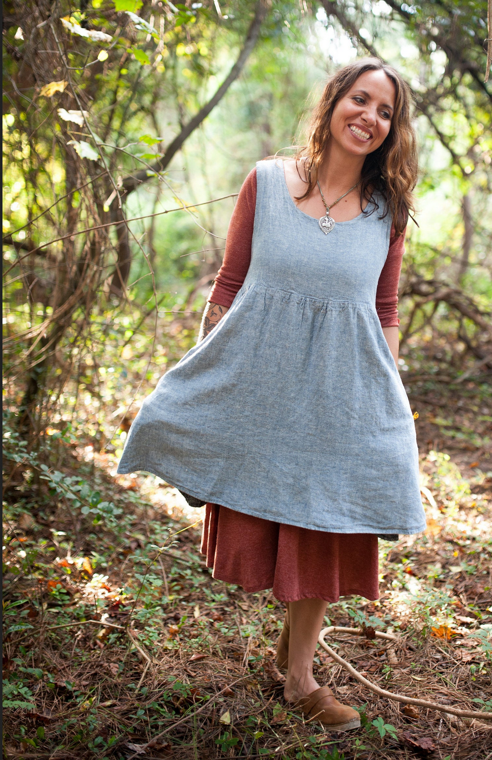 Woman in a light blue dress over a brown dress standing in a forest