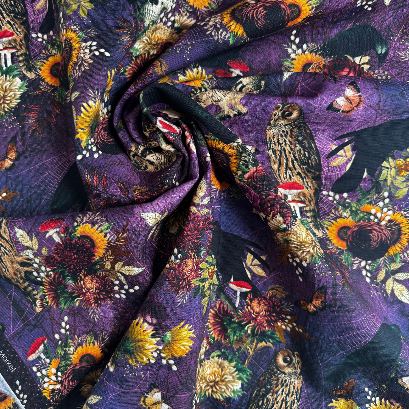 Close-up of Robert Kaufman Dreadful Delights fabric in midnight purple, showing a detailed spooky gothic design with realistic skulls, ravens, owls, spiderwebs, and dark floral arrangements.