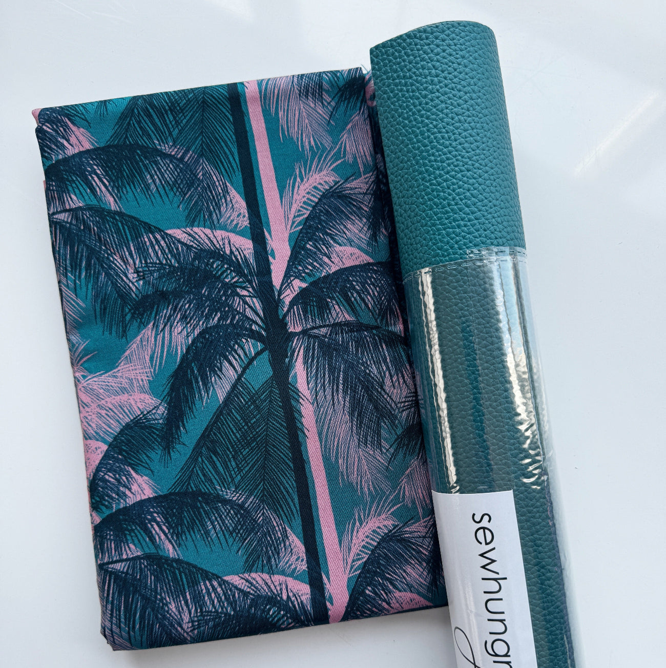 A flat-lay view of the craft materials for the Match Up #3 package, showing a folded piece of Ruby Star fabric with a palm tree pattern next to a rolled sheet of teal textured vinyl labeled "sewhungryhippie".