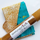 A flat-lay view of the craft materials for the Match Up #4 package, showing a roll of mustard-yellow faux suede with a "sewhungryhippie" label, alongside folded pieces of teal fabric and animal-print lining fabric.