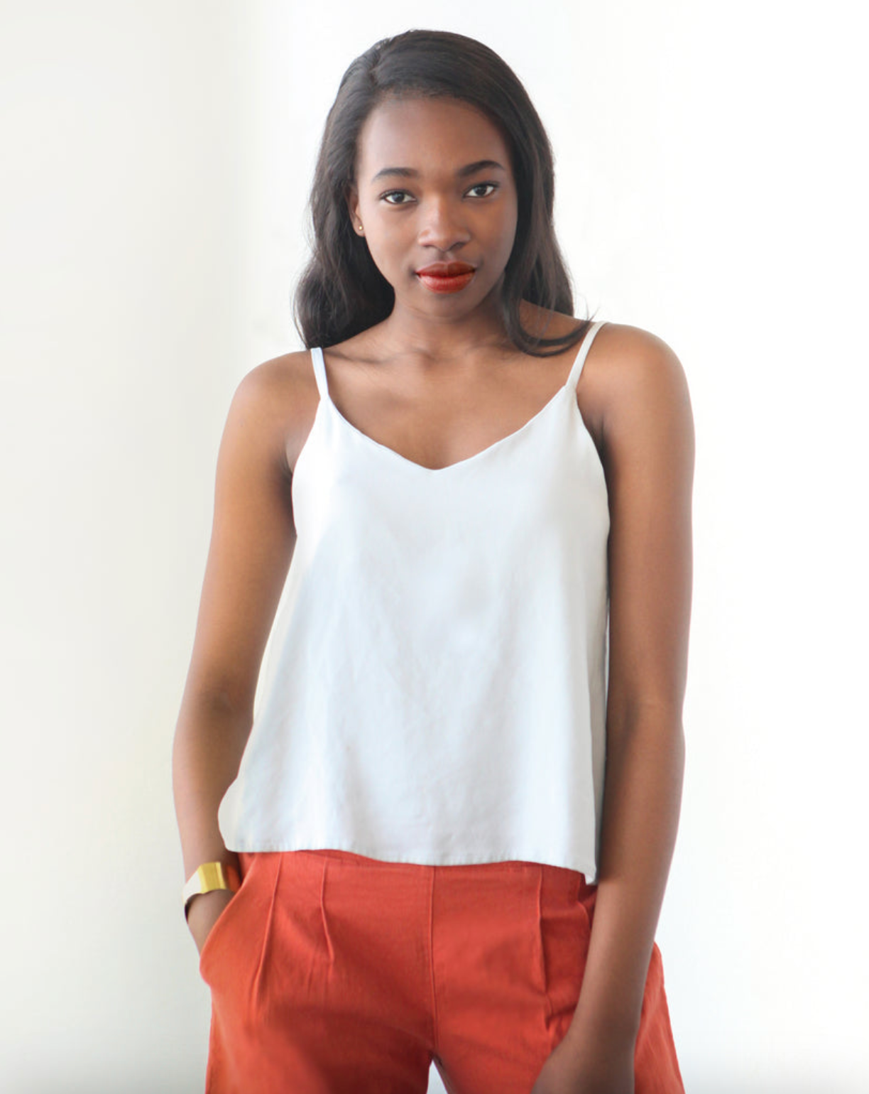 Woman wearing a white top and orange pants against a white background