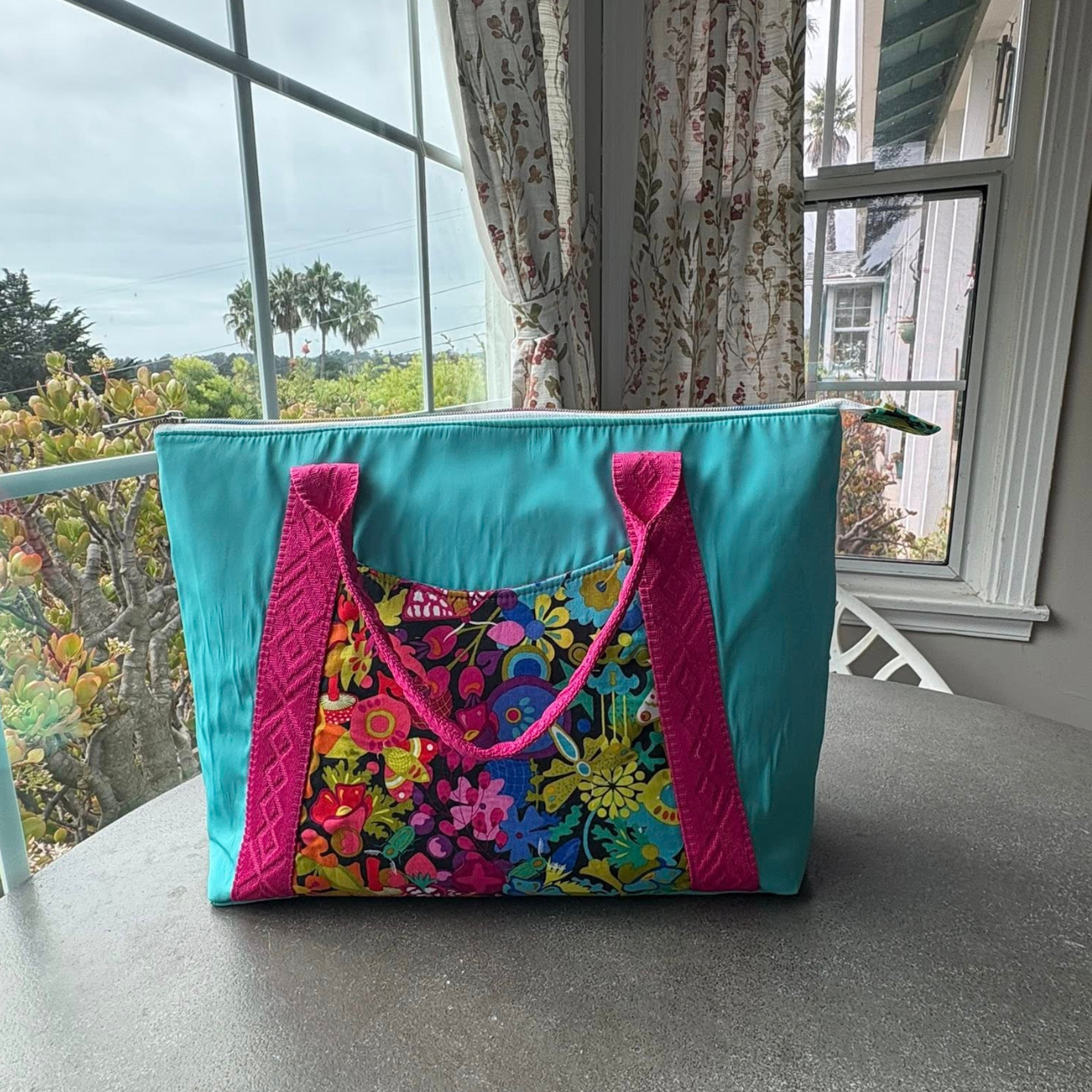 Large handmade turquoise zipper-top tote bag featuring a colorful abstract floral exterior pocket panel and hot pink geometric diamond jacquard webbing handles