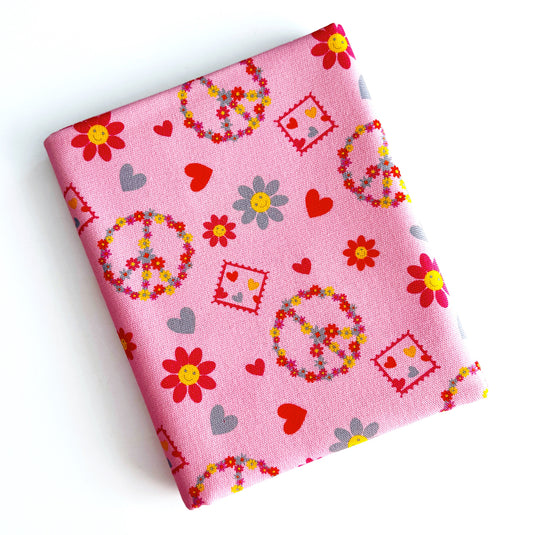 Pink fabric with a retro pattern of peace signs, hearts, and flowers, shown folded on a white background.