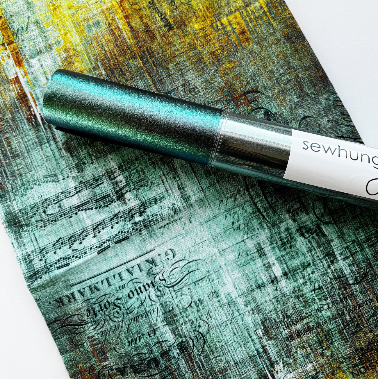 A yard of distressed teal and ochre sheet music canvas fabric paired with a coordinating roll of moonglow iridescent teal vinyl.