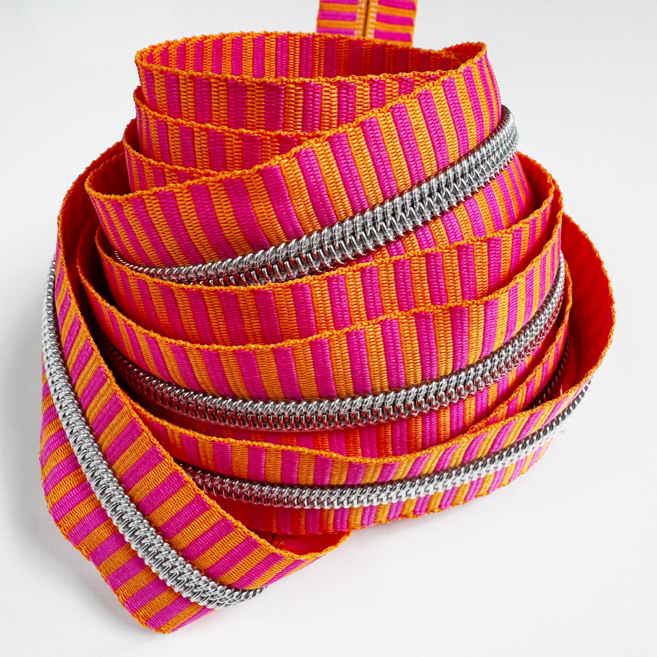 Number 5 continuous zipper tape featuring a bright pink and orange jacquard woven stripe pattern with metallic silver coil teeth, coiled neatly against a white background.